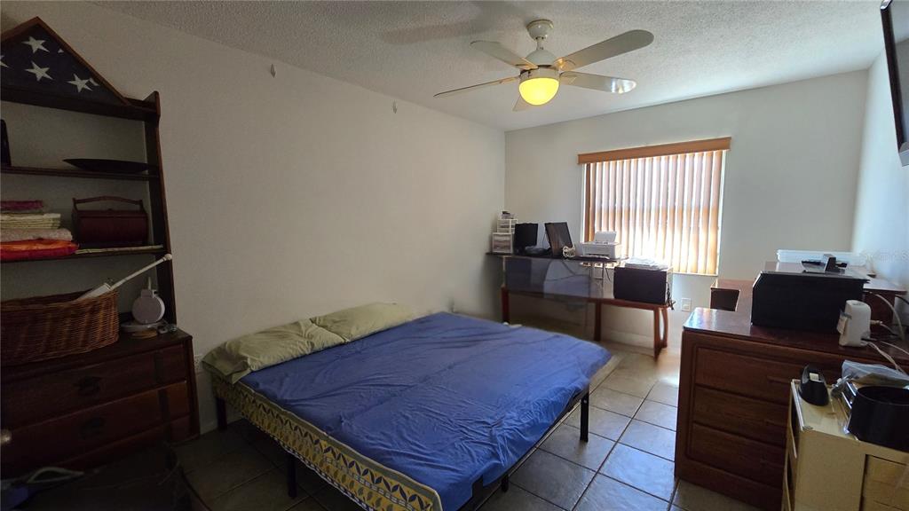 A bedroom features a bed with a blue cover, a ceiling fan, and wooden furniture — 4628 ASHBERRY DRIVE, SARASOTA, FL