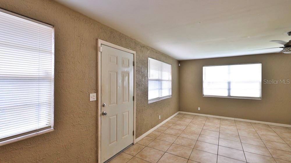 An empty room features beige walls, tiled flooring, a white entry door, and three windows — 347 PLEASANT STREET, DAYTONA BEACH, FL