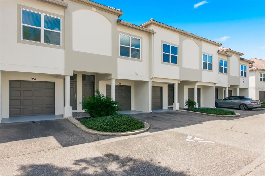 A row of multi-story townhomes with attached garages and paved driveways under a blue sky — 1027 NORMANDY TRACE ROAD, TAMPA, FL