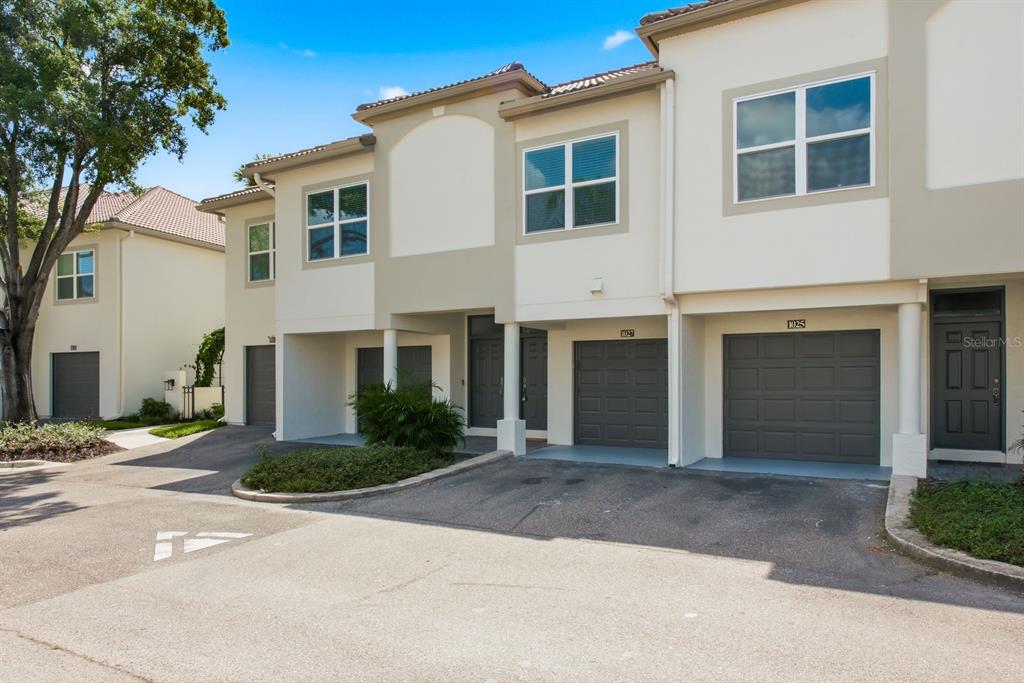 A row of multi-story townhomes with gray garage doors and beige stucco exteriors — 1027 NORMANDY TRACE ROAD, TAMPA, FL