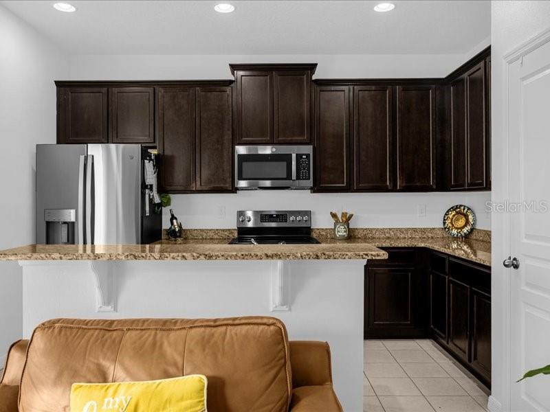 A kitchen with dark wood cabinets, granite countertops, and stainless steel appliances overlooks a living area — 1020 UMBRIA LANE, ST CLOUD, FL