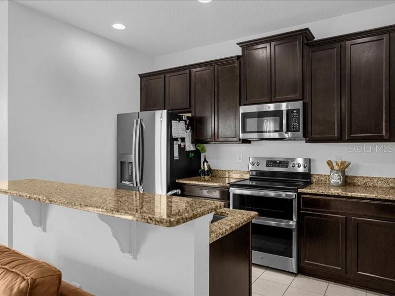A kitchen with dark wood cabinets, granite countertops, stainless steel appliances, and a breakfast bar — 1020 UMBRIA LANE, ST CLOUD, FL
