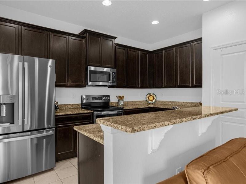 A kitchen features dark wood cabinets, granite countertops, and stainless steel appliances — 1020 UMBRIA LANE, ST CLOUD, FL