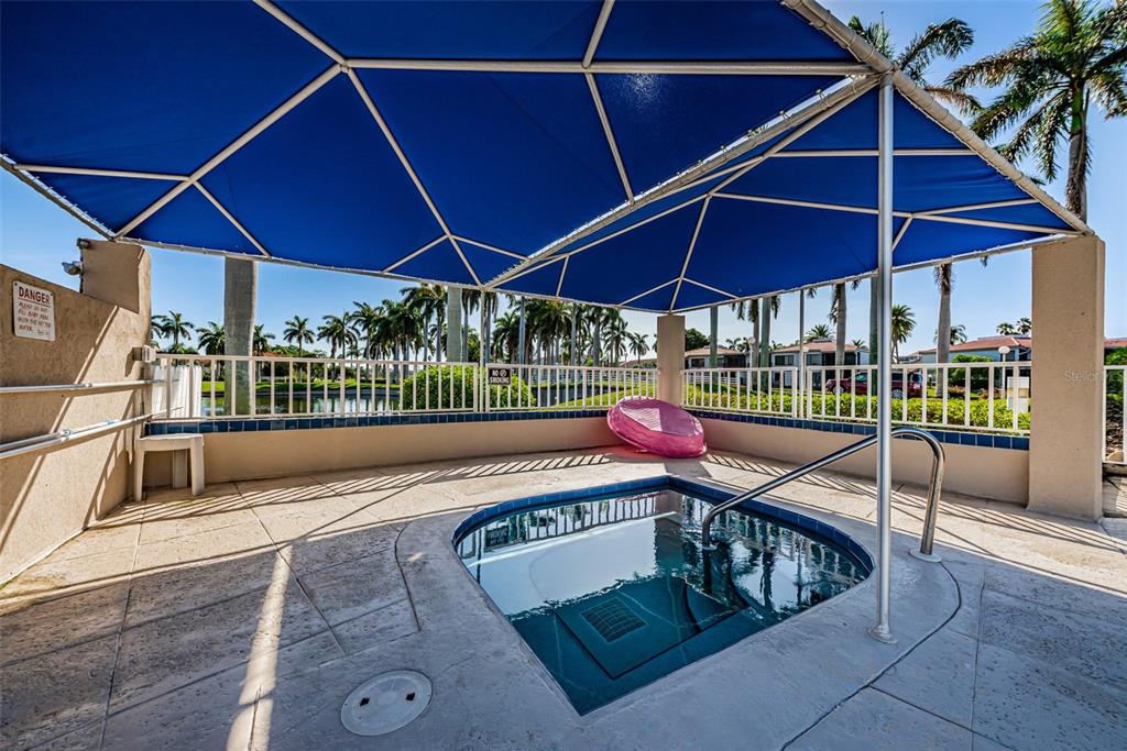 A square hot tub sits on a tiled patio under a large blue shade canopy — 6000 BAHIA DEL MAR CIRCLE UNIT 130, ST PETERSBURG, FL