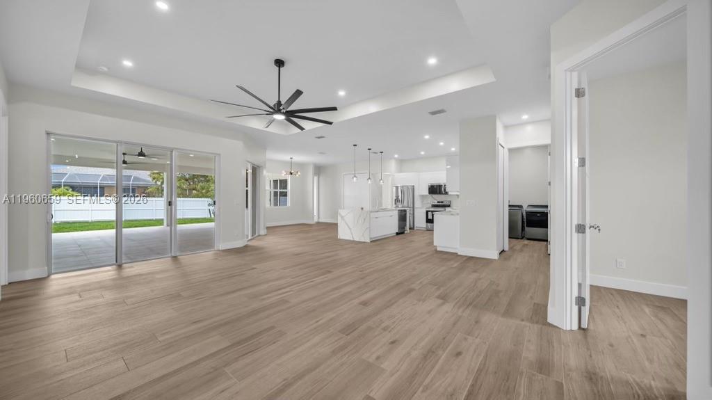 An open-concept living area features light wood-look flooring, a tray ceiling, and a modern kitchen — 1726 SW 36TH TER,, Cape Coral FL 33914, CAPE CORAL, FL