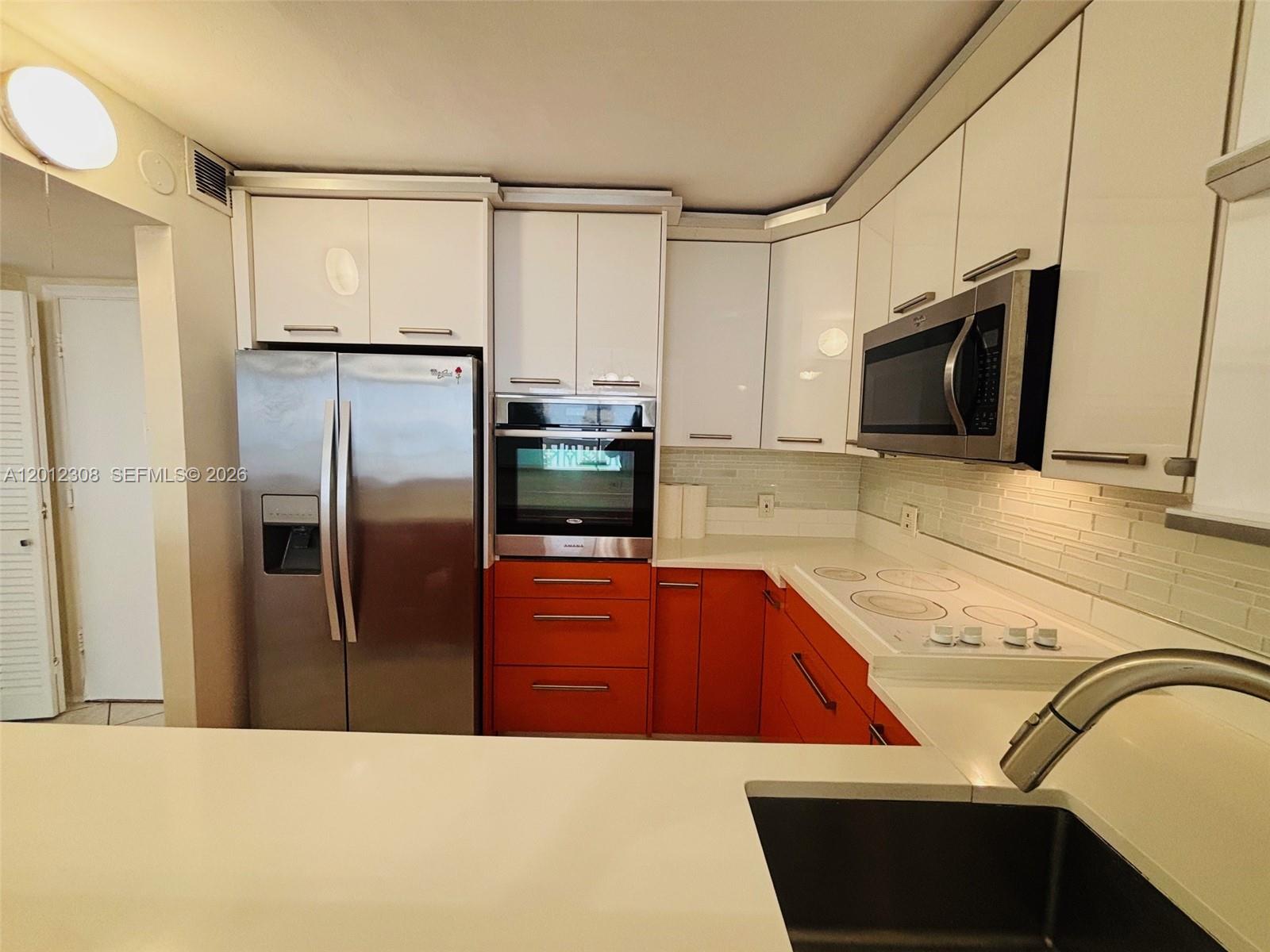 A kitchen features white upper cabinets, orange lower cabinets, stainless steel appliances, and white countertops — 1817 S Ocean Dr # 622, Hallandale Beach FL 33009, HALLANDALE BEACH, FL