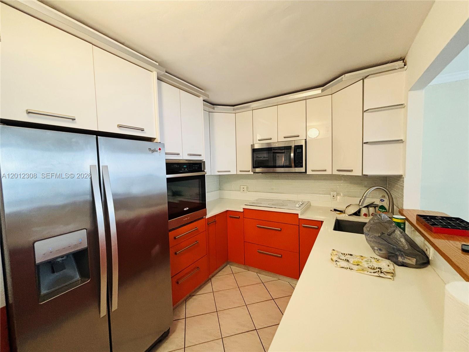 A kitchen features orange lower cabinets, white upper cabinets, stainless steel appliances, and white countertops — 1817 S Ocean Dr # 622, Hallandale Beach FL 33009, HALLANDALE BEACH, FL