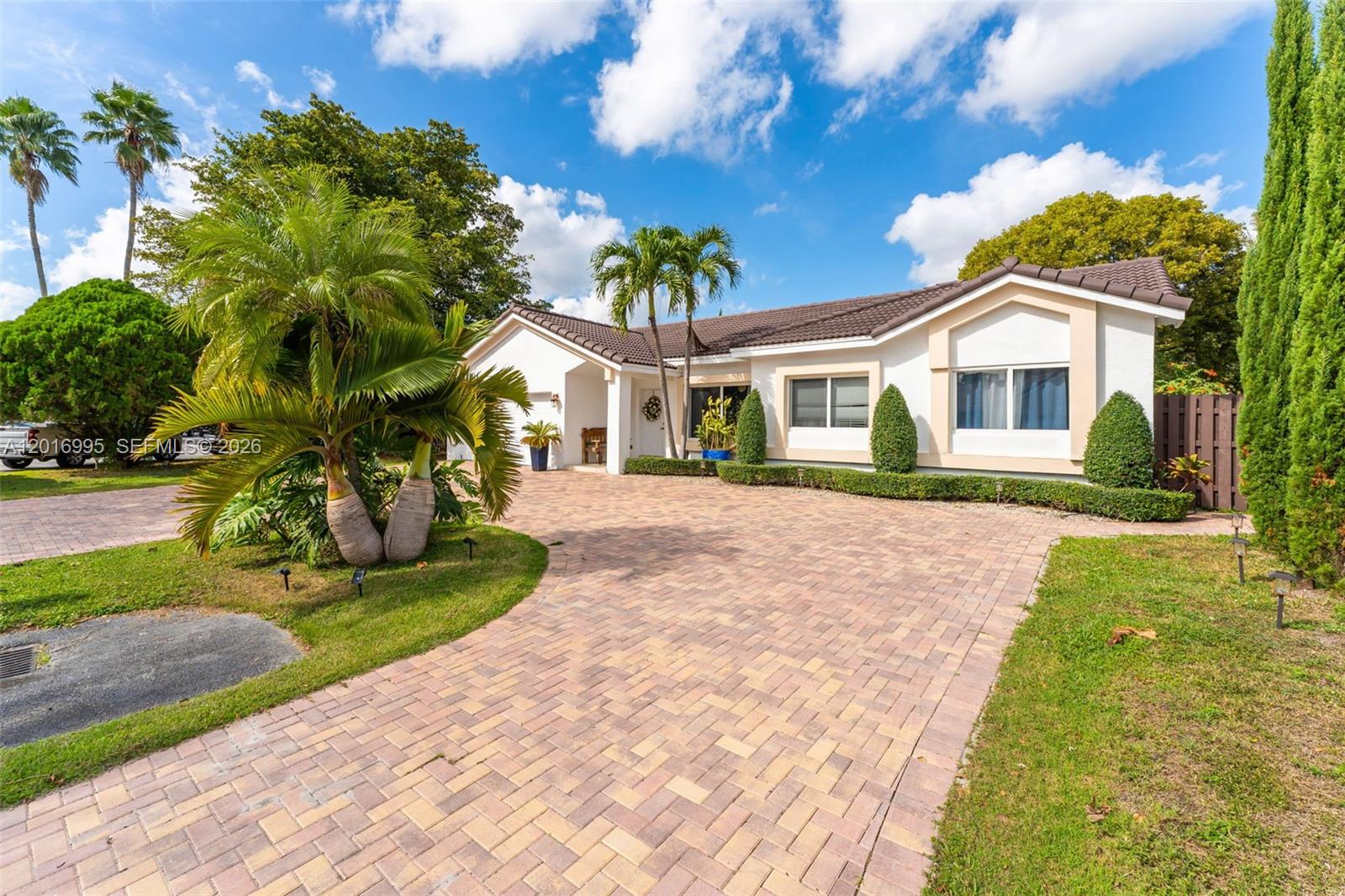 A single-story house with a brick paver driveway and palm trees under a blue sky — 15325 SW 54th Ter, Miami FL 33185, MIAMI, FL