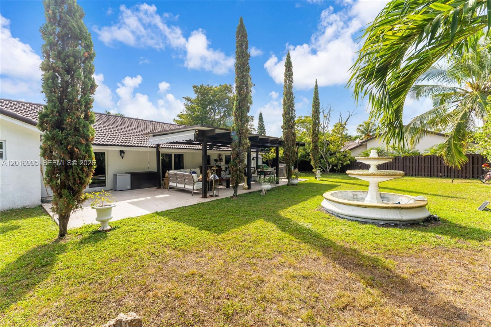 A backyard features a patio with a pergola, a tiered fountain, and tall cypress trees — 15325 SW 54th Ter, Miami FL 33185, MIAMI, FL