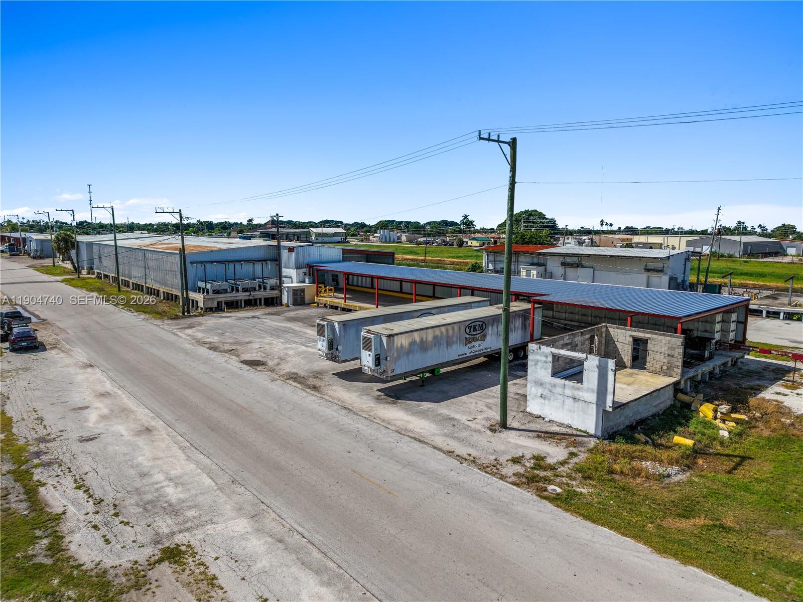 An aerial view shows an industrial warehouse facility with parked semi-trailers and a paved road — 901 NW 9th St, Belle Glade FL 33430, BELLE GLADE, FL