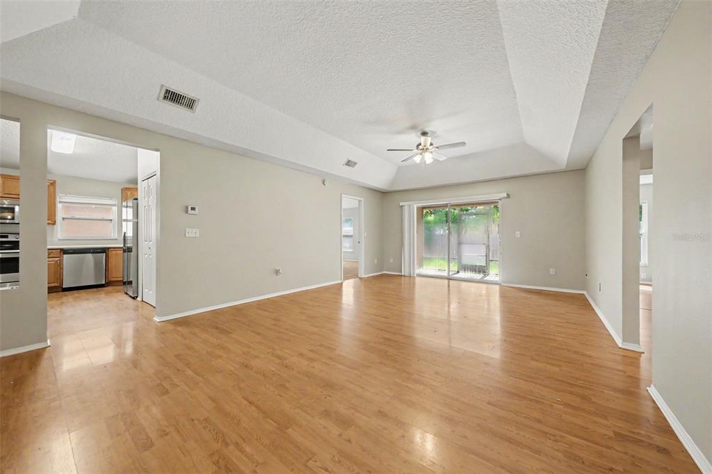 A spacious living room with light wood flooring, a tray ceiling, and a sliding glass door — 1077 SUGARBERRY TRAIL, OVIEDO, FL