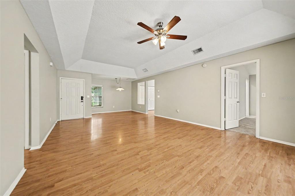 An empty living room with light wood flooring, a tray ceiling, and a ceiling fan — 1077 SUGARBERRY TRAIL, OVIEDO, FL