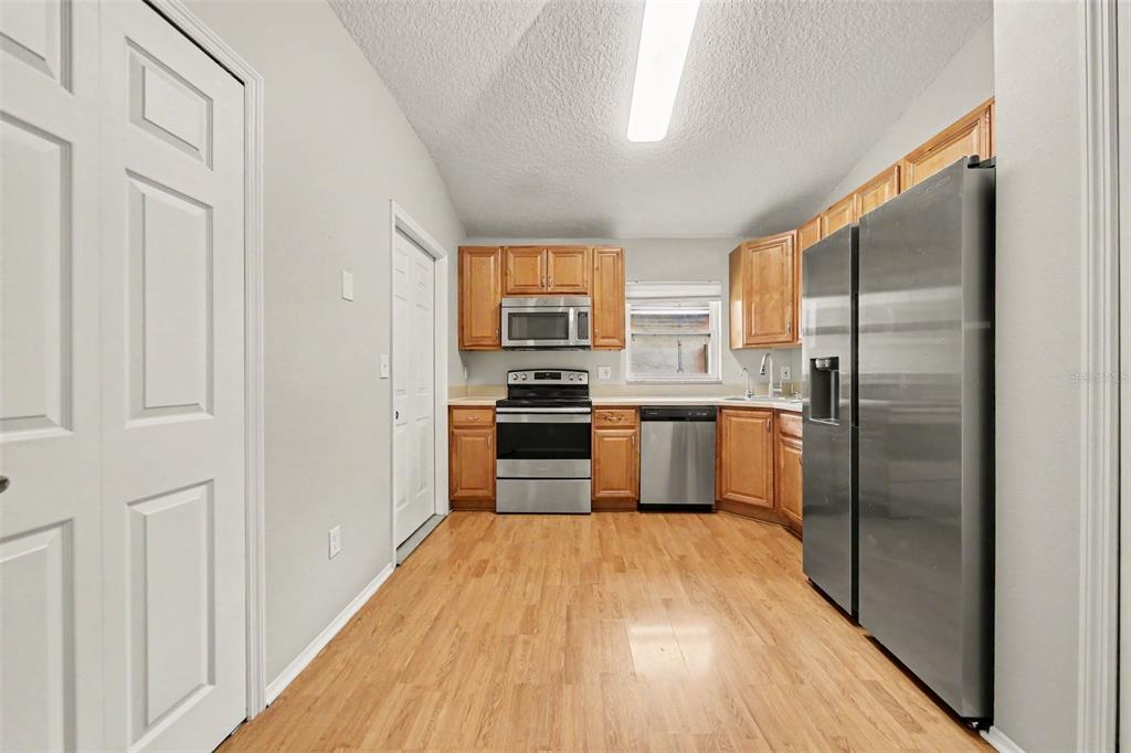A kitchen features light wood cabinets, stainless steel appliances, and light-colored wood-look flooring — 1077 SUGARBERRY TRAIL, OVIEDO, FL