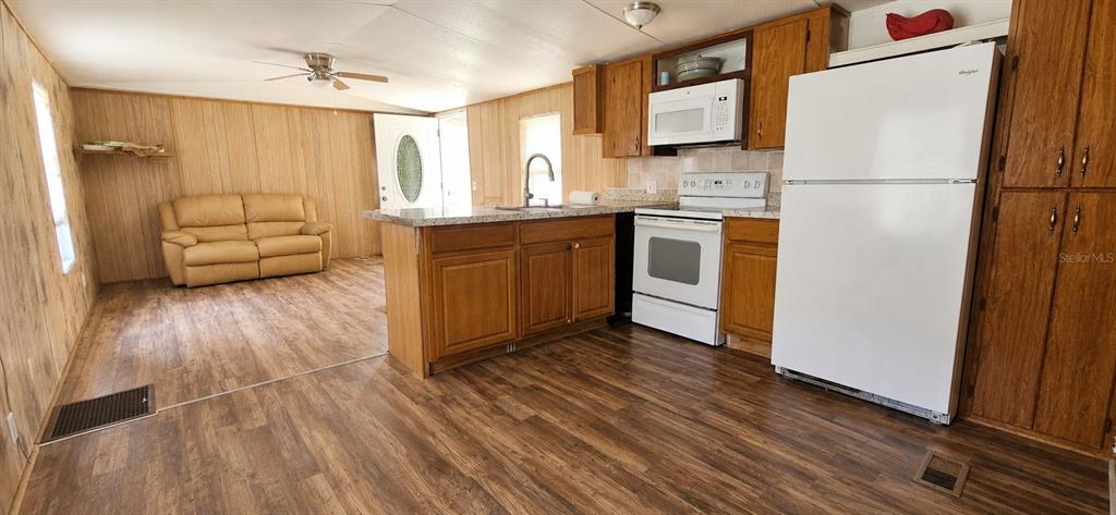 A kitchen with wood cabinets and a white refrigerator opens into a living area — 706 DAVID AVENUE, INTERLACHEN, FL
