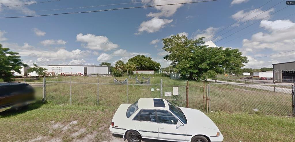 A white car is parked in front of a fenced, grassy vacant lot with trees — 60 E STREET, LAKE WALES, FL