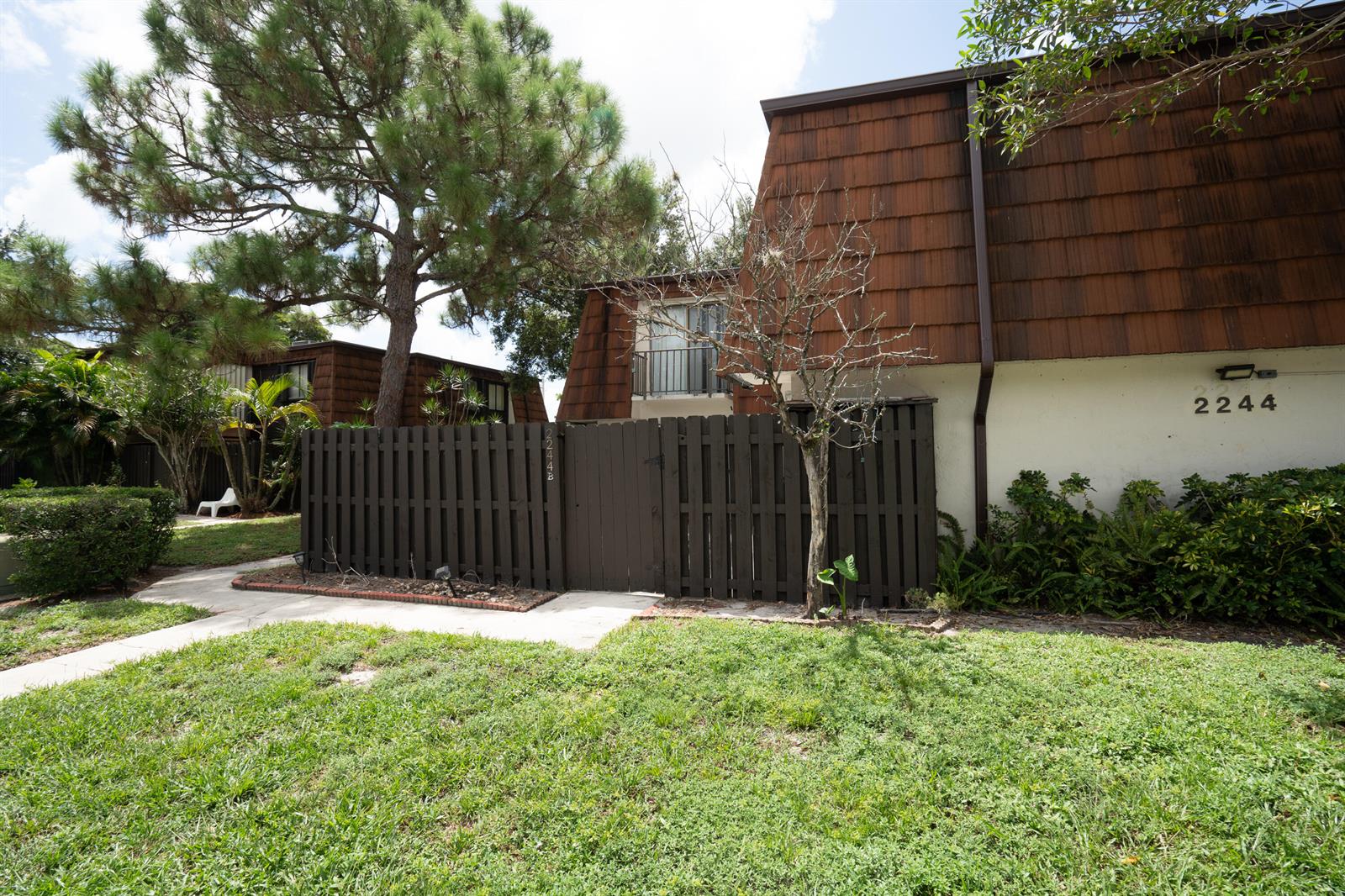 An exterior view shows a brown wooden fence, a bare tree, and a shingled building — 2244 White Pine Circle # B, FL 33415, FL
