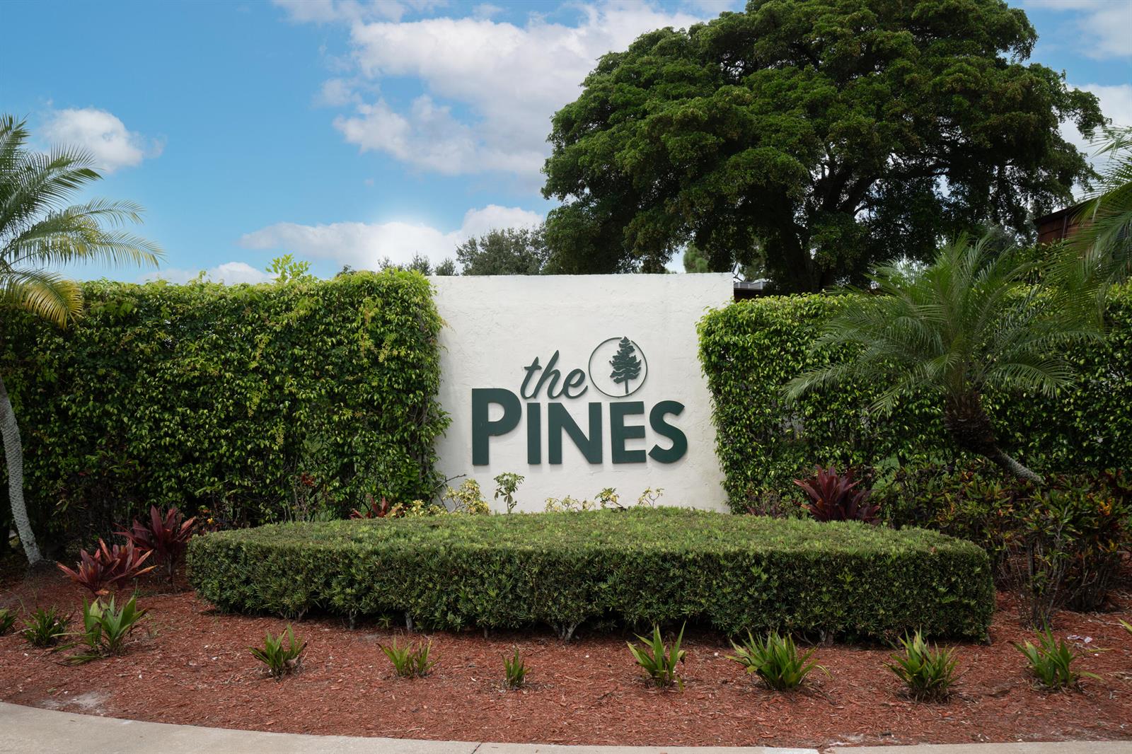 A white sign reading "the PINES" stands behind a manicured hedge and landscaped garden — 2244 White Pine Circle # B, FL 33415, FL