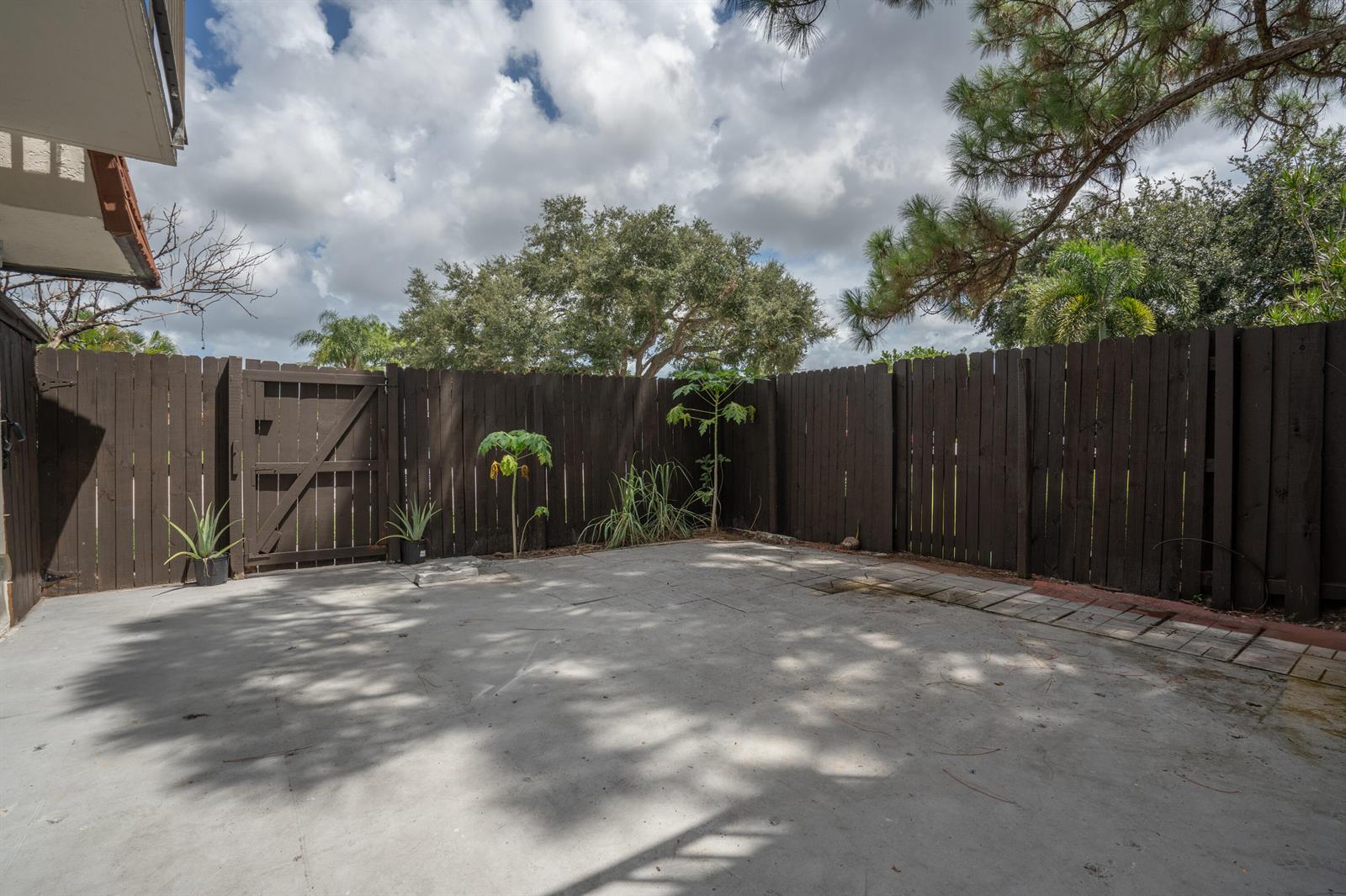 A concrete patio enclosed by a dark wooden fence with a gate and small plants — 2244 White Pine Circle # B, FL 33415, FL