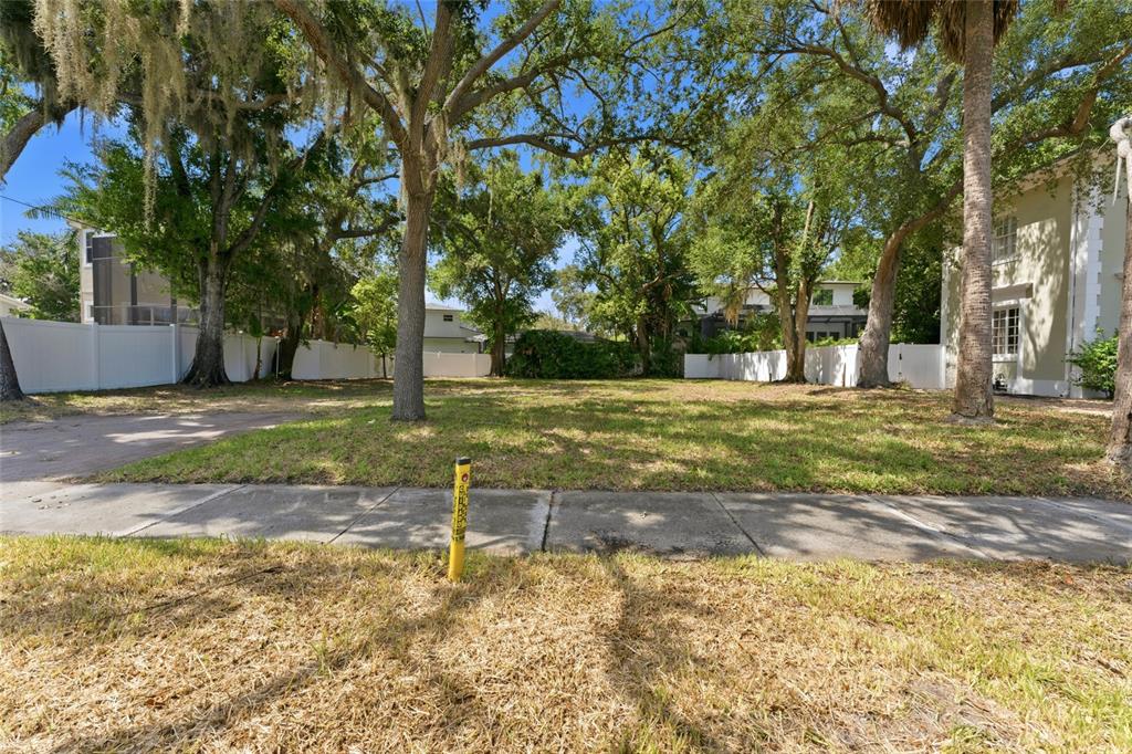 A vacant, grassy residential lot features mature trees and a white vinyl privacy fence — 5010 W AZEELE STREET, TAMPA, FL