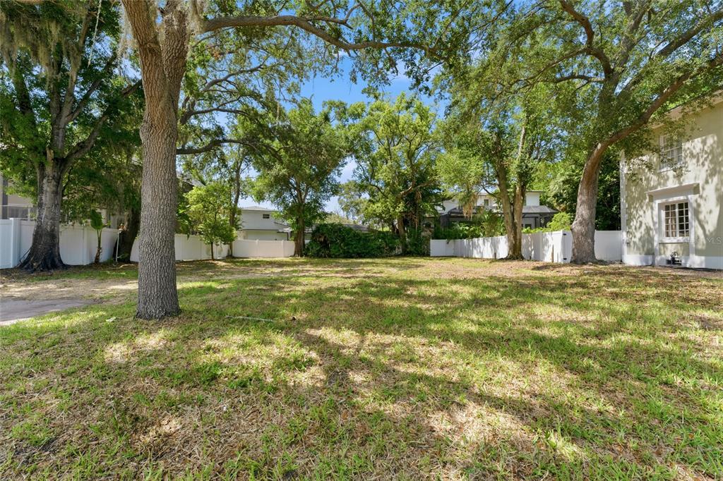 A grassy, tree-filled vacant lot is enclosed by white vinyl fencing between two houses — 5010 W AZEELE STREET, TAMPA, FL