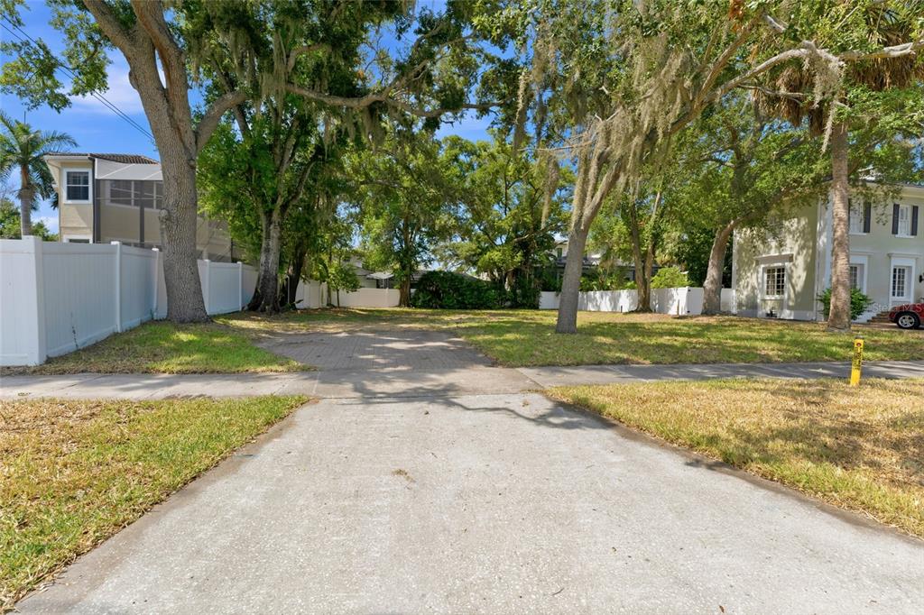A vacant residential lot features a paved driveway, mature trees, and white perimeter fencing — 5010 W AZEELE STREET, TAMPA, FL