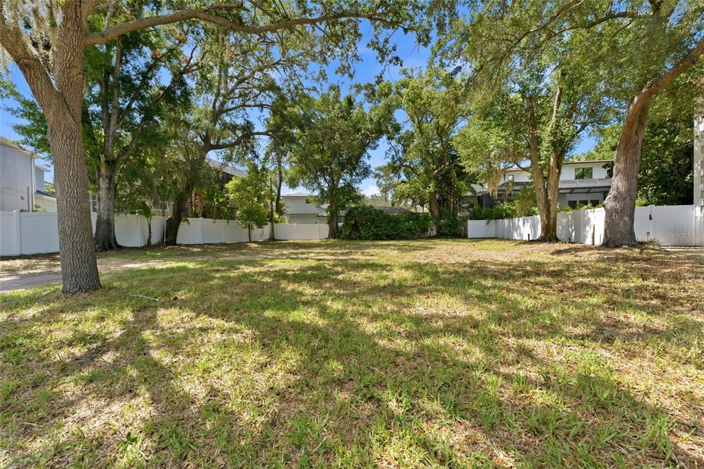A grassy, vacant residential lot is enclosed by a white vinyl fence and mature trees — 5010 W AZEELE STREET, TAMPA, FL