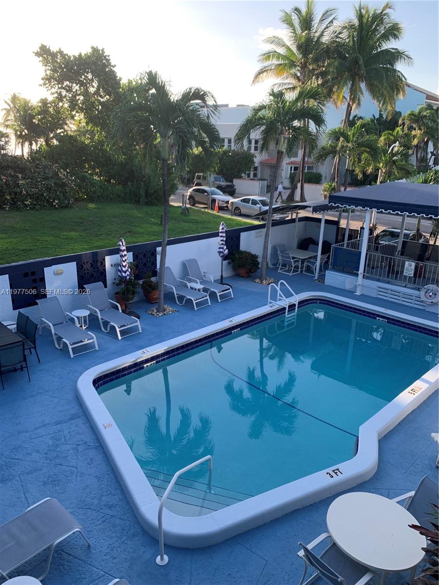 An outdoor swimming pool area features lounge chairs, umbrellas, and palm trees on a patio — 322 Taylor St # 2D, Hollywood FL 33019, HOLLYWOOD, FL