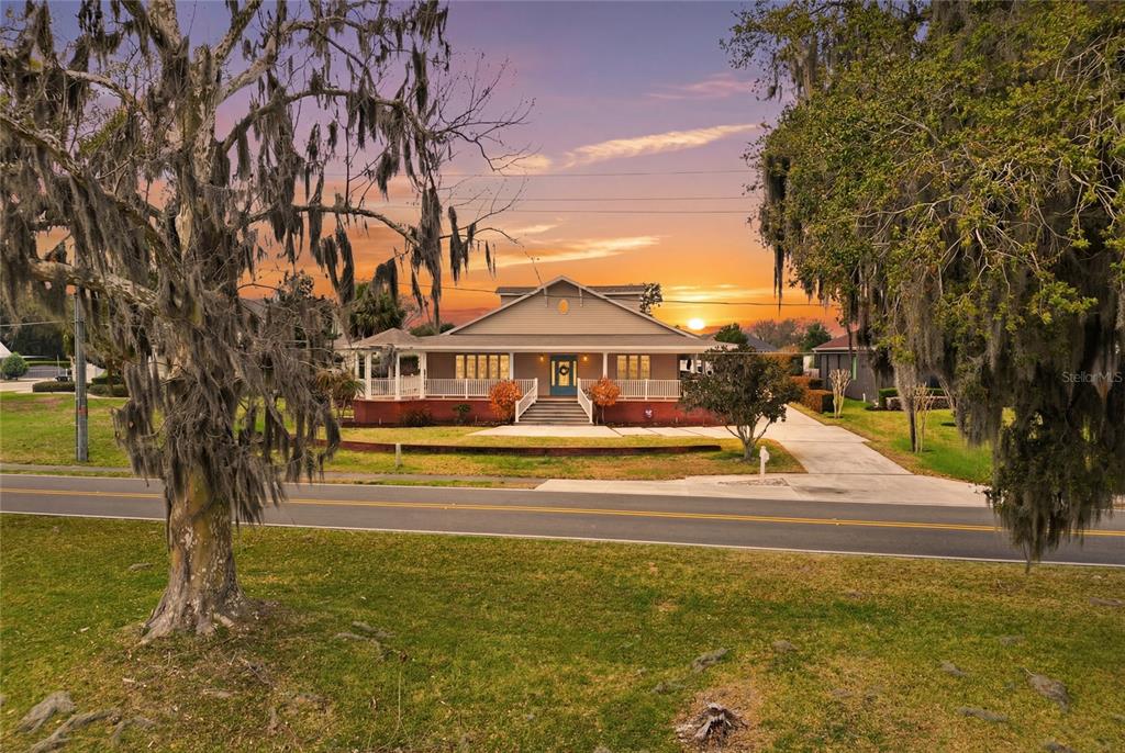 A single-story house with a wide front porch sits behind a road and large trees — 2128 LAKE ARIANA BOULEVARD, AUBURNDALE, FL
