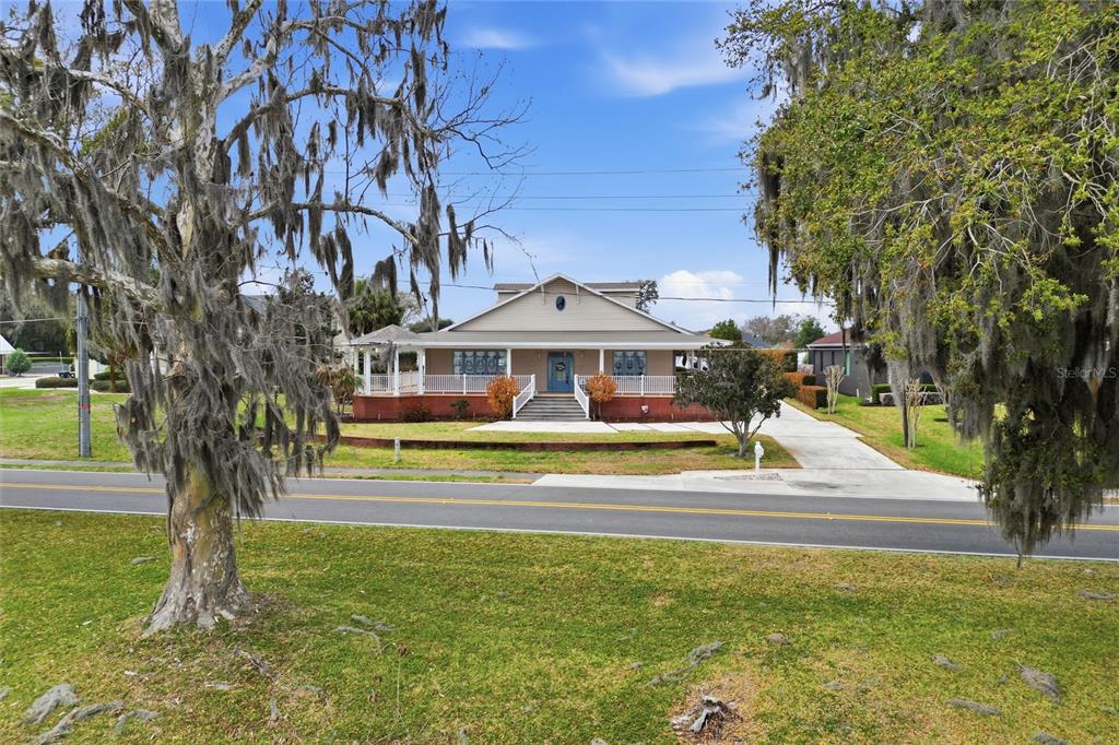 A single-story house with a wrap-around porch sits behind a road and large trees — 2128 LAKE ARIANA BOULEVARD, AUBURNDALE, FL