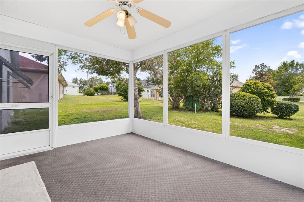 A screened-in porch with gray carpeting, a ceiling fan, and large windows overlooking a yard — 660 W SUNSET STRIP DRIVE, BEVERLY HILLS, FL