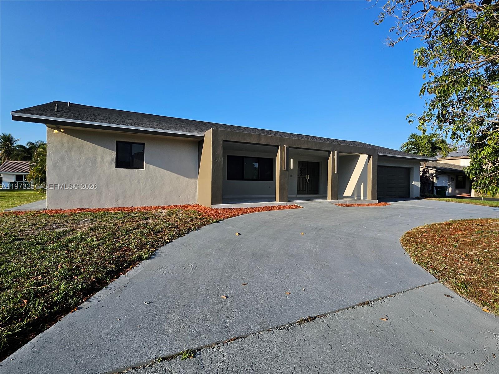 A single-story house with a gray driveway, a covered entryway, and a dark garage door — 11761 NW 27th Ct, Plantation FL 33323, PLANTATION, FL