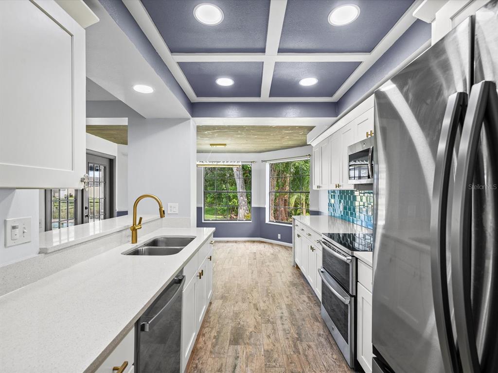 A kitchen features white cabinets, quartz countertops, a blue coffered ceiling, and wood-look flooring — 3827 WATSON DRIVE, NEW PORT RICHEY, FL