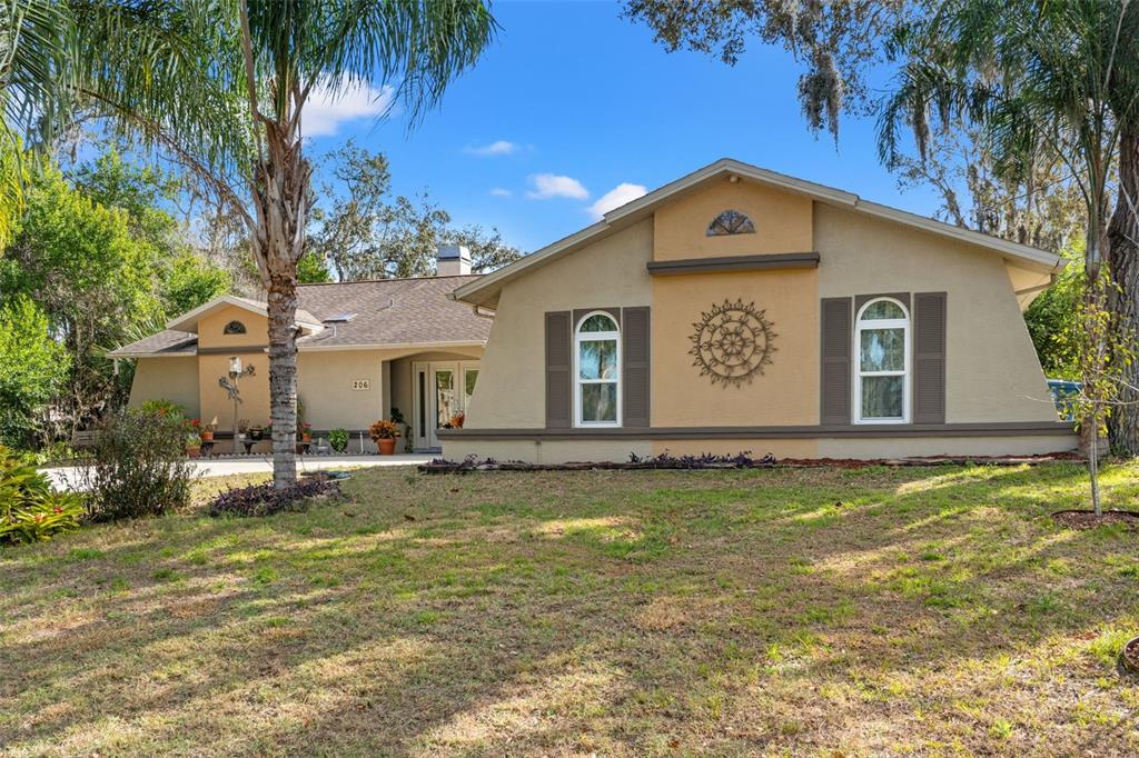 A single-story house with a tan stucco exterior, brown shutters, and a front lawn — 206 RUSK CIRCLE, SPRING HILL, FL