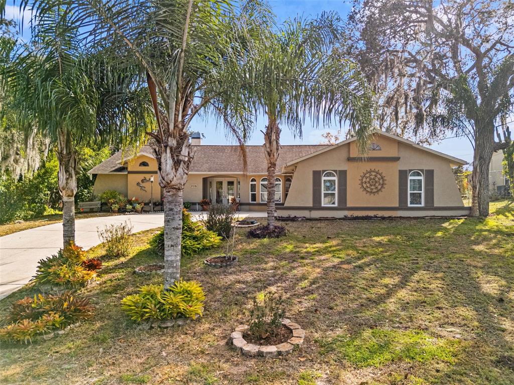 A single-story house with a tan exterior, palm trees, and a front lawn — 206 RUSK CIRCLE, SPRING HILL, FL