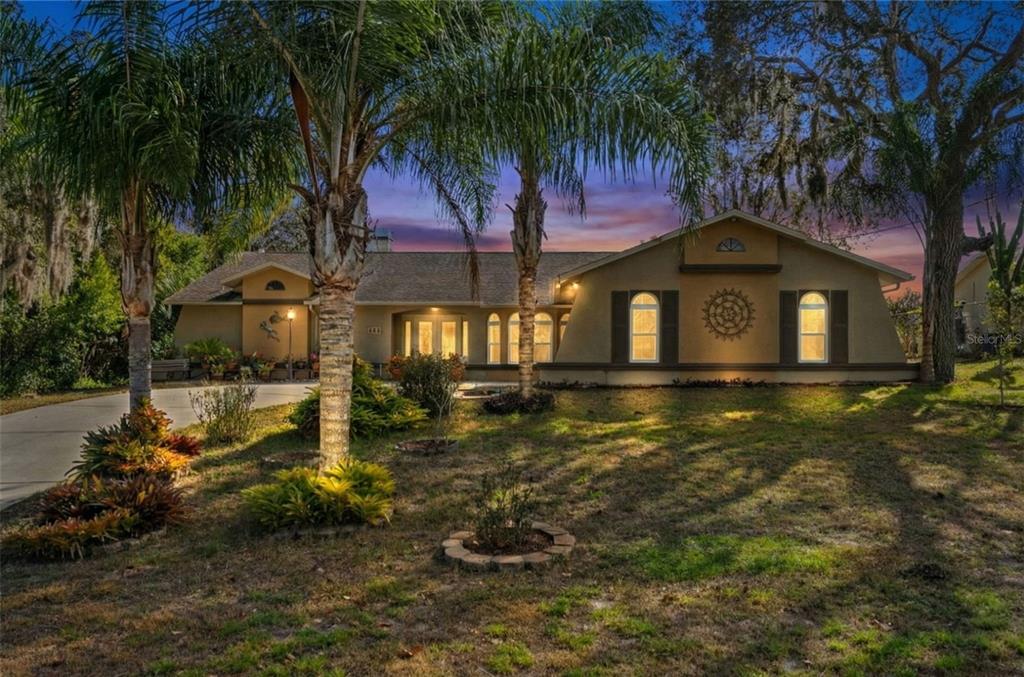 A single-story house with a tan stucco exterior, arched windows, and palm trees at dusk — 206 RUSK CIRCLE, SPRING HILL, FL