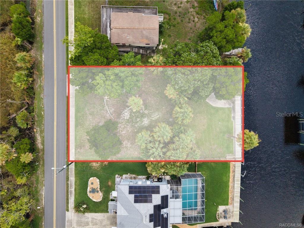 An aerial view shows a vacant, tree-covered waterfront lot outlined in red between two houses — 2020 NW 19TH STREET, CRYSTAL RIVER, FL