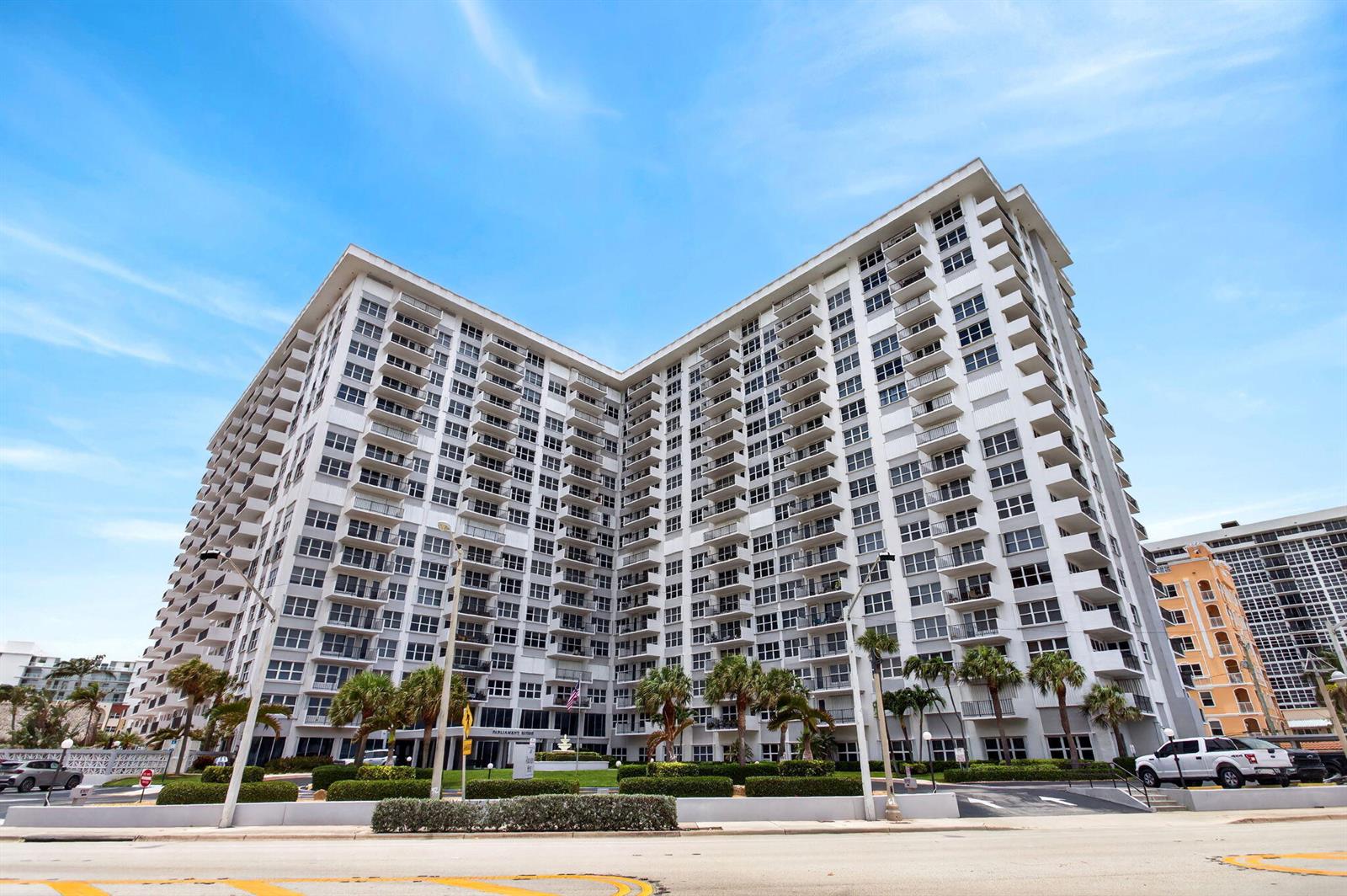 A low-angle exterior view of a large, multi-story white apartment building with many balconies — 405 N Ocean Boulevard # 507, Pompano Beach FL 33062, POMPANO BEACH, FL