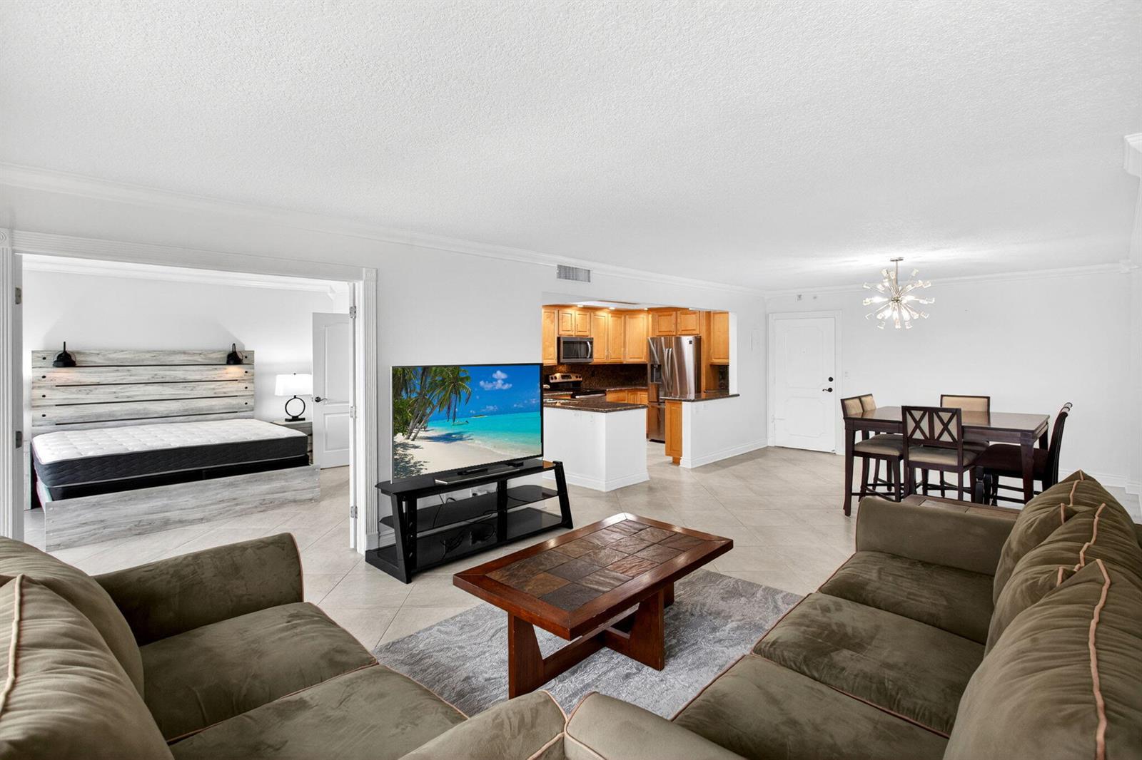 A living room with a brown sofa, coffee table, and television, opening to a bedroom — 405 N Ocean Boulevard # 507, Pompano Beach FL 33062, POMPANO BEACH, FL