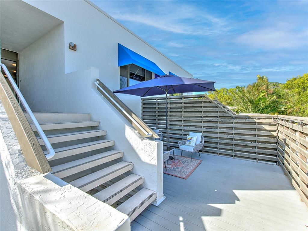 An outdoor staircase leads to a deck with a blue umbrella and wooden privacy fencing — 805 BAYPORT WAY UNIT 805, LONGBOAT KEY, FL