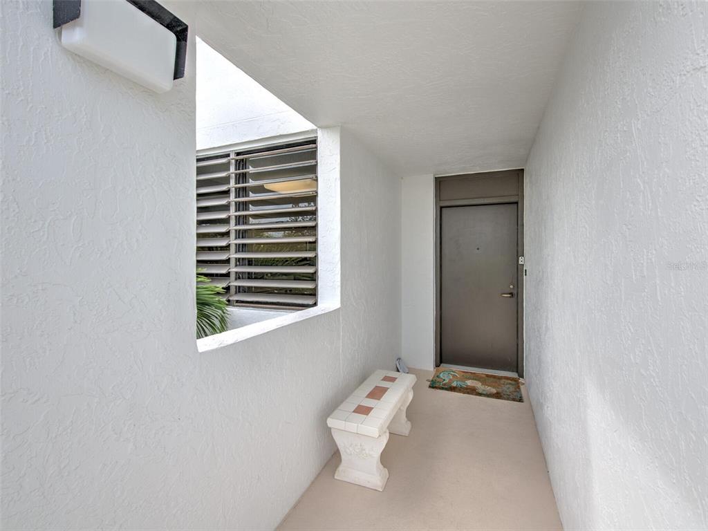 A covered entryway features a white bench, a brown door, and a louvered window — 805 BAYPORT WAY UNIT 805, LONGBOAT KEY, FL