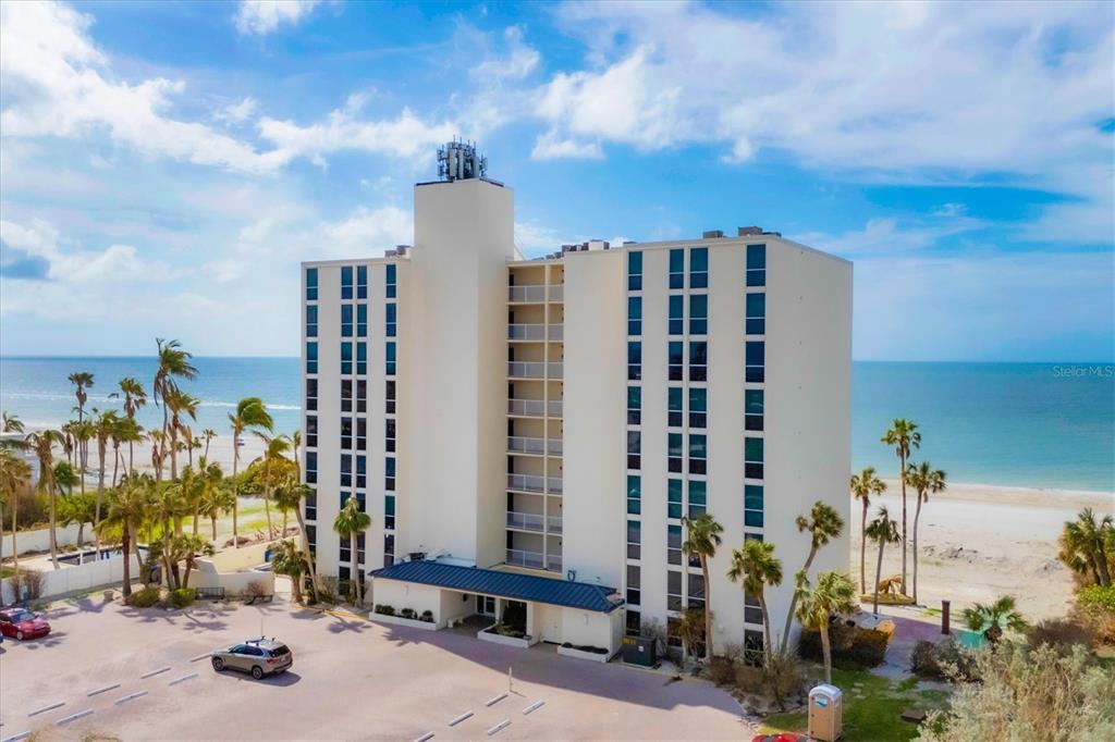 An aerial view of a multi-story beachfront condominium building with a parking lot and palm trees — 4485 GULF OF MEXICO DRIVE UNIT PH2, LONGBOAT KEY, FL