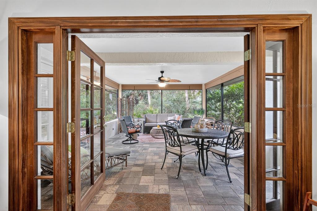 A view through wooden French doors into a screened-in patio with stone flooring and furniture — 29 SAN JOSE DRIVE, PALM COAST, FL