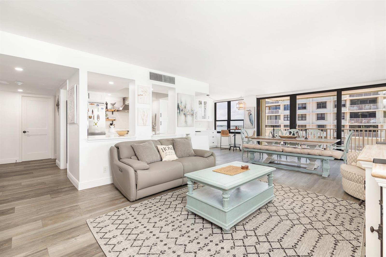 A living and dining area with light wood floors, a gray sofa, and balcony views — 5480 N Ocean Drive, Riviera Beach FL 33404, RIVIERA BEACH, FL