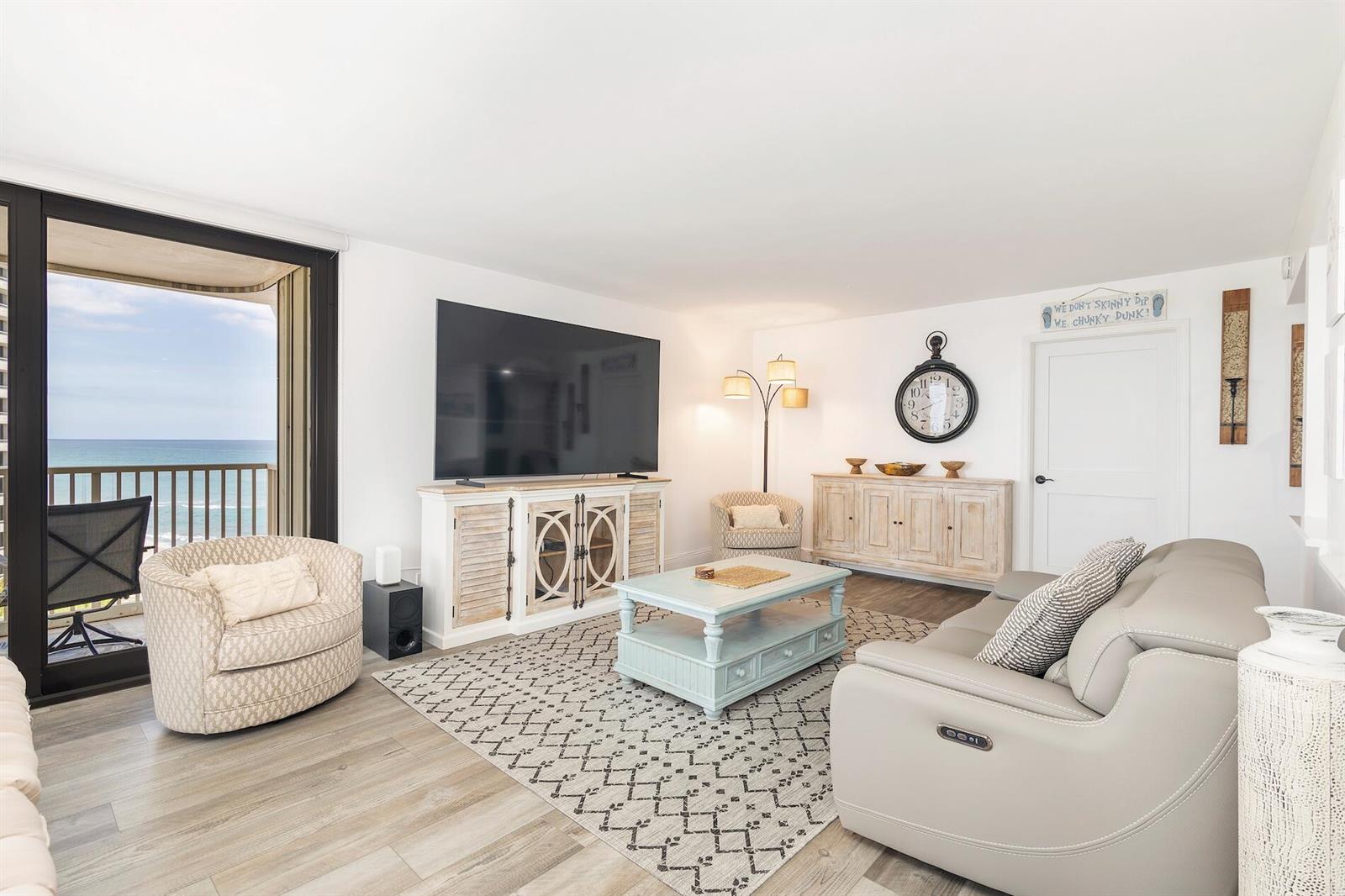 A living room features a large television, light-colored furniture, a patterned rug, and balcony views — 5480 N Ocean Drive, Riviera Beach FL 33404, RIVIERA BEACH, FL