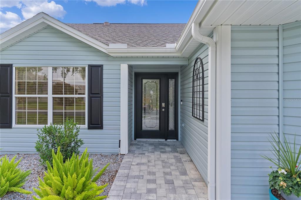 The exterior of a light blue house features a paved walkway leading to a front door — 1795 HAGOOD LOOP, THE VILLAGES, FL