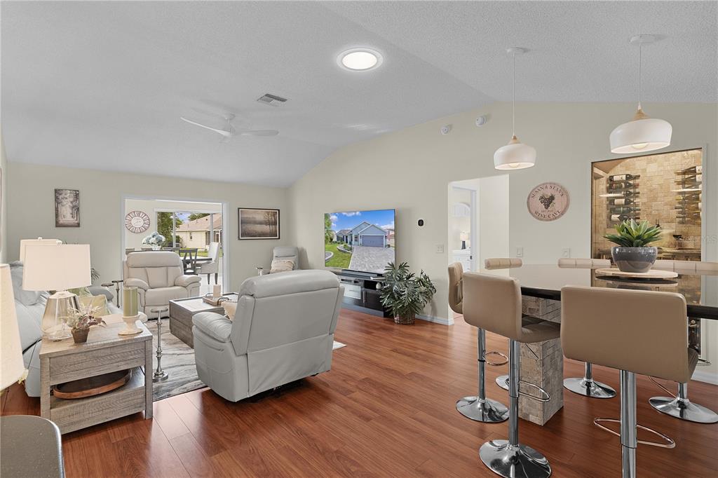 A living room and kitchen bar area with wood flooring, light-colored furniture, and a wine display — 1795 HAGOOD LOOP, THE VILLAGES, FL