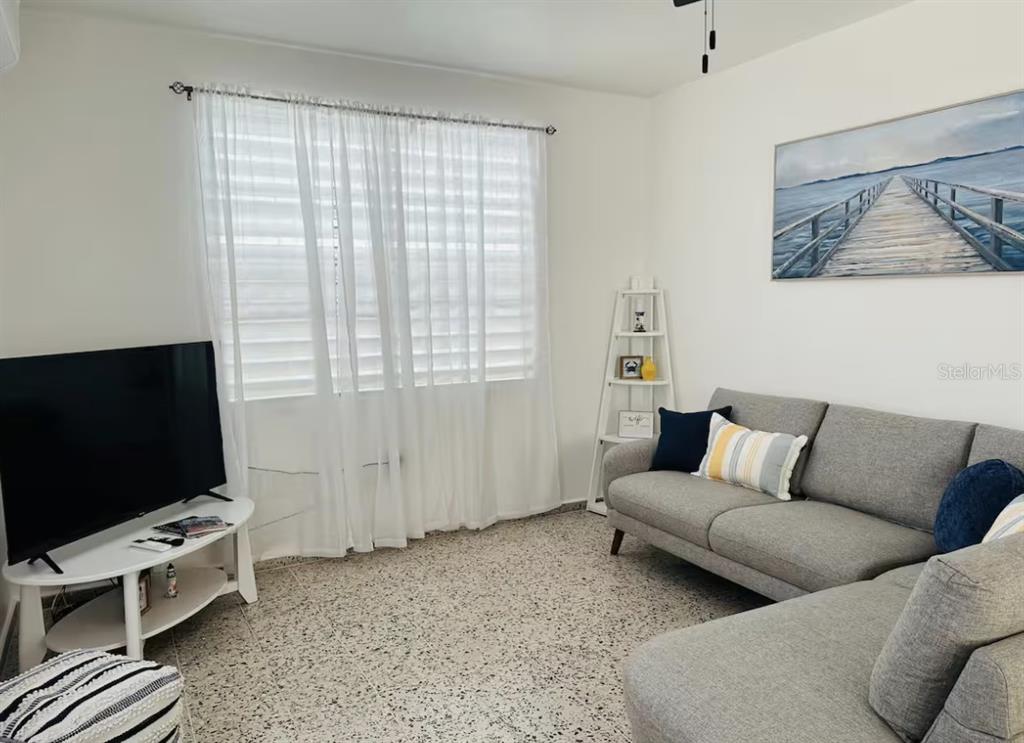 A living room features a gray sectional sofa, a television on a stand, and terrazzo flooring — Calle II 2 3301 COMBATE, BOQUERON, PR