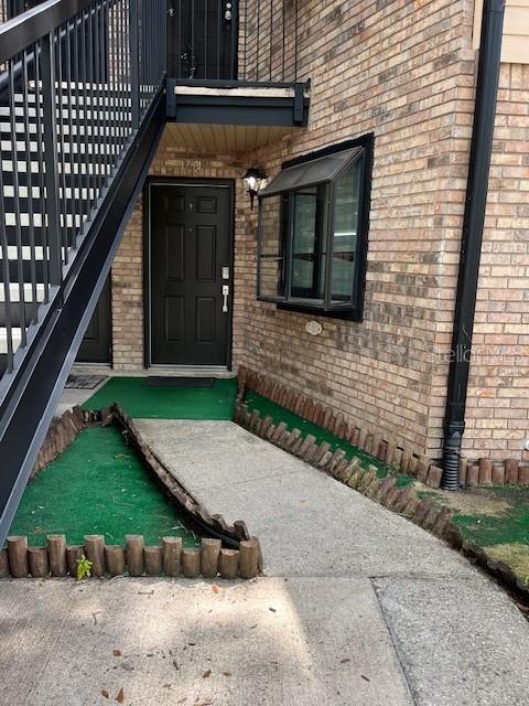A brick building exterior features a black front door, a bay window, and metal stairs — 1734 FOXHALL CIRCLE UNIT -, KISSIMMEE, FL