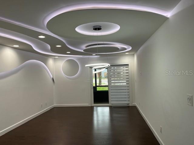 An empty room features dark wood flooring and a modern ceiling with recessed lighting and curves — 1734 FOXHALL CIRCLE UNIT -, KISSIMMEE, FL
