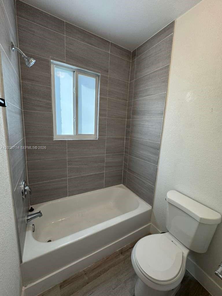 A bathroom features a white bathtub, a toilet, and gray horizontal wall tiles — MIAMI, FL